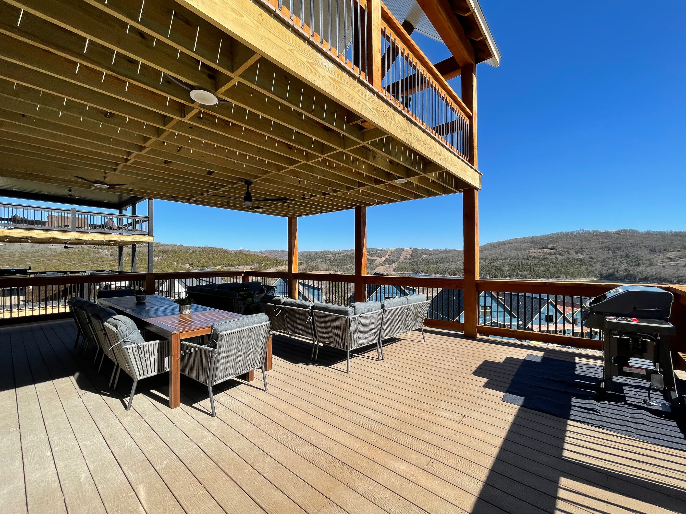 Main level deck with gas grill, comfy sectional couch, and table with chairs.