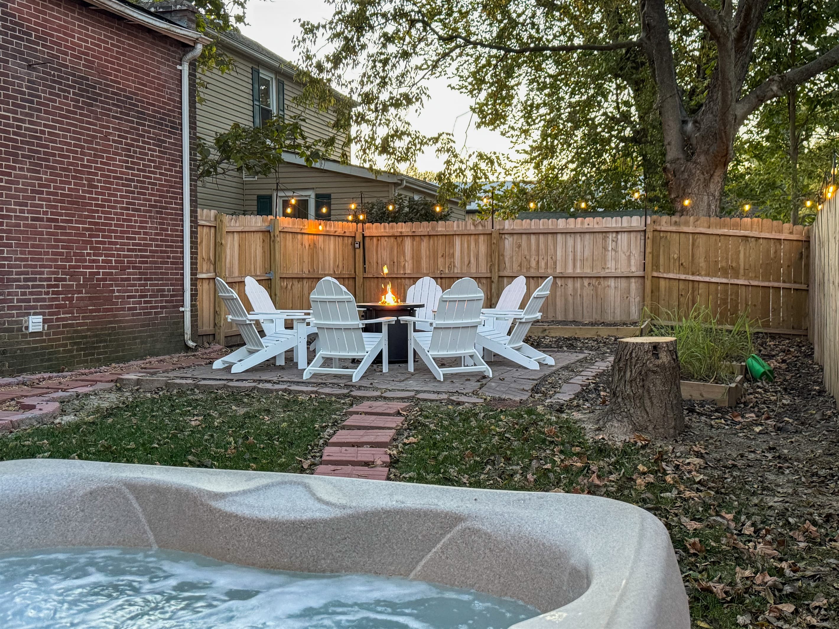 Private fenced in yard with propane fire pit, and stone walkway between hot tub and patio.