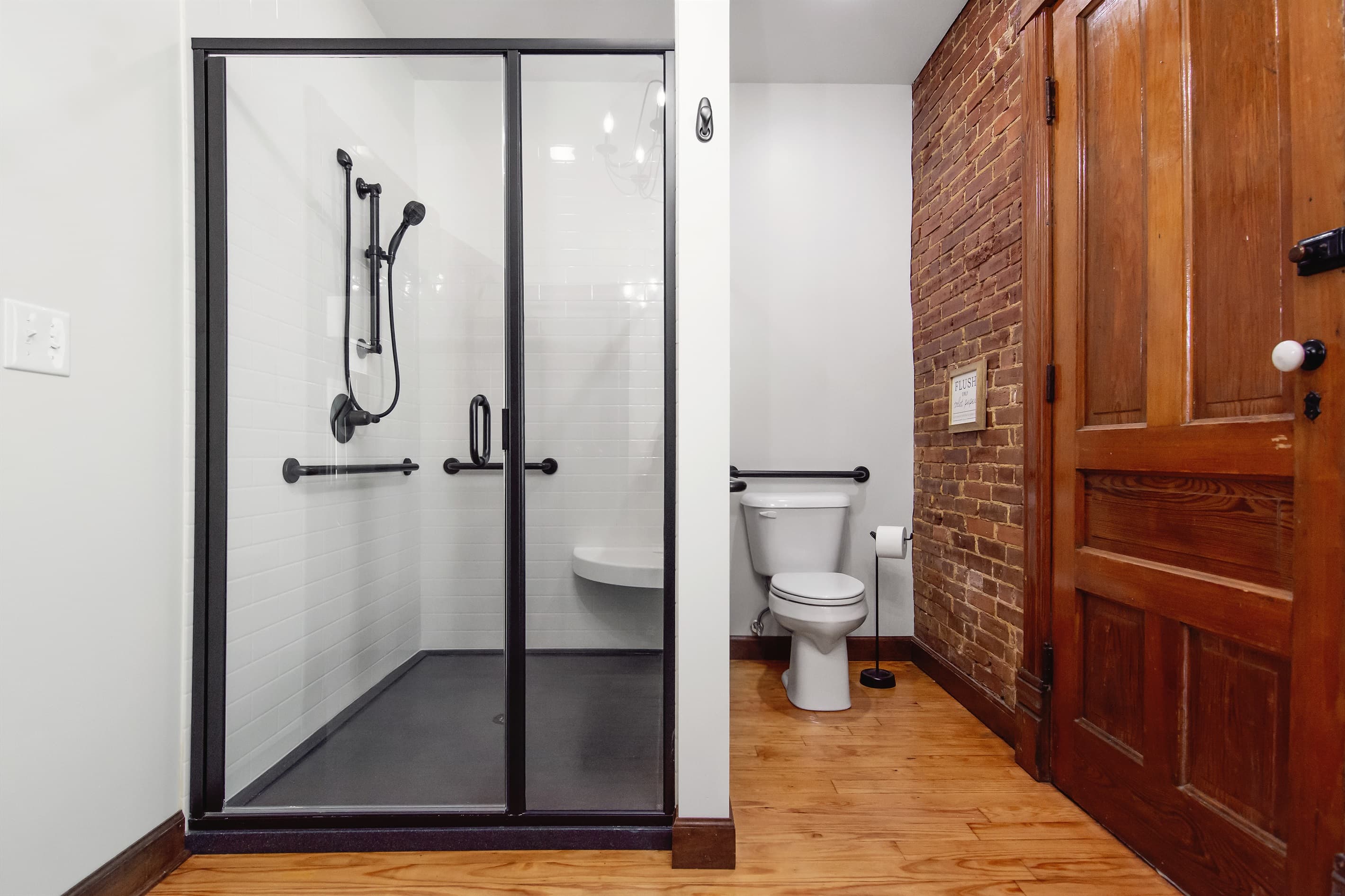 Spacious stand up shower with bench, grab bars, and hand held shower head.