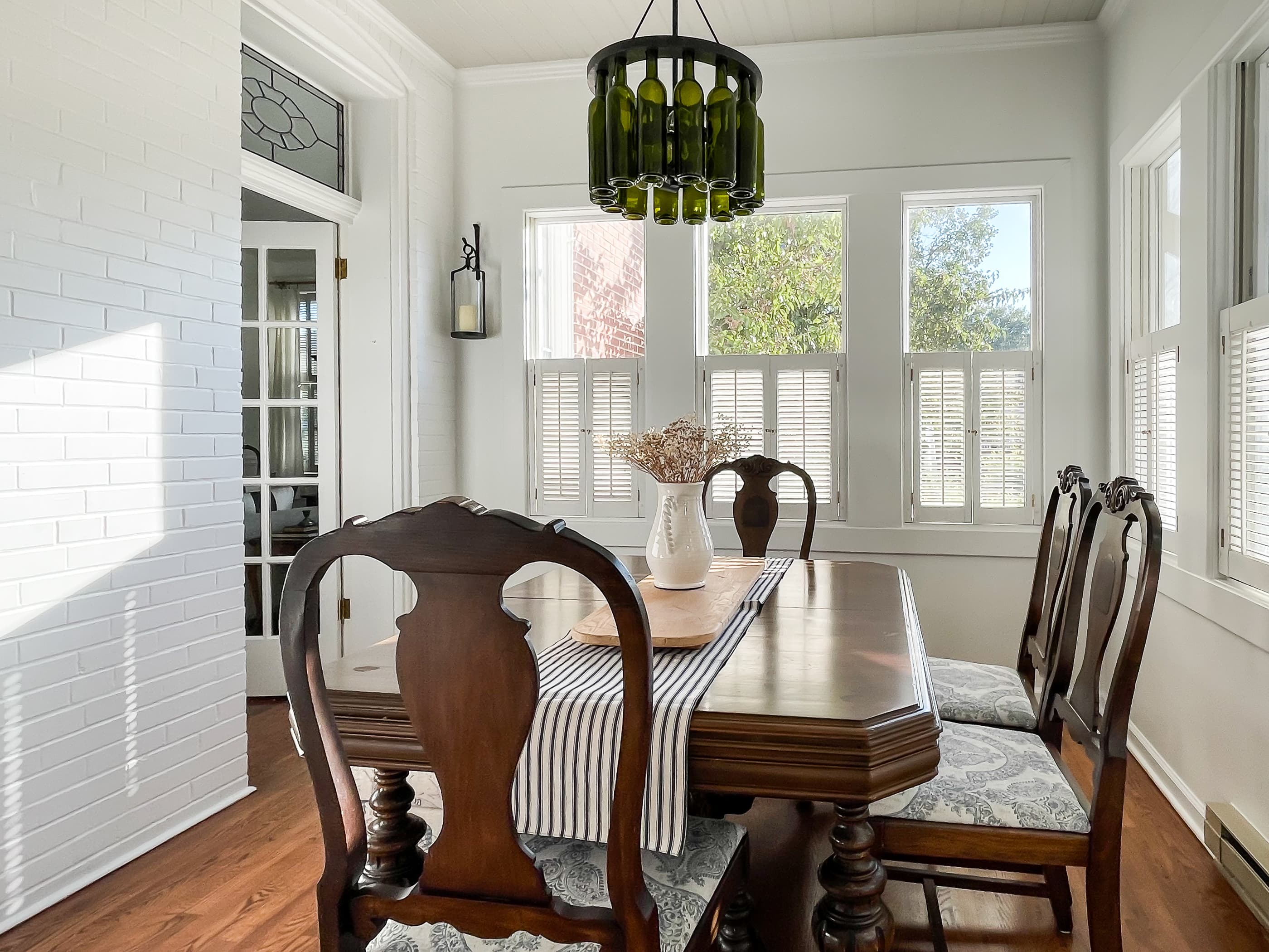 The dining area in the Mill Haus Sunroom seats 6 people and features a unique green wine bottle chandelier, with additional seating in the kitchen and on the screened back porch. 