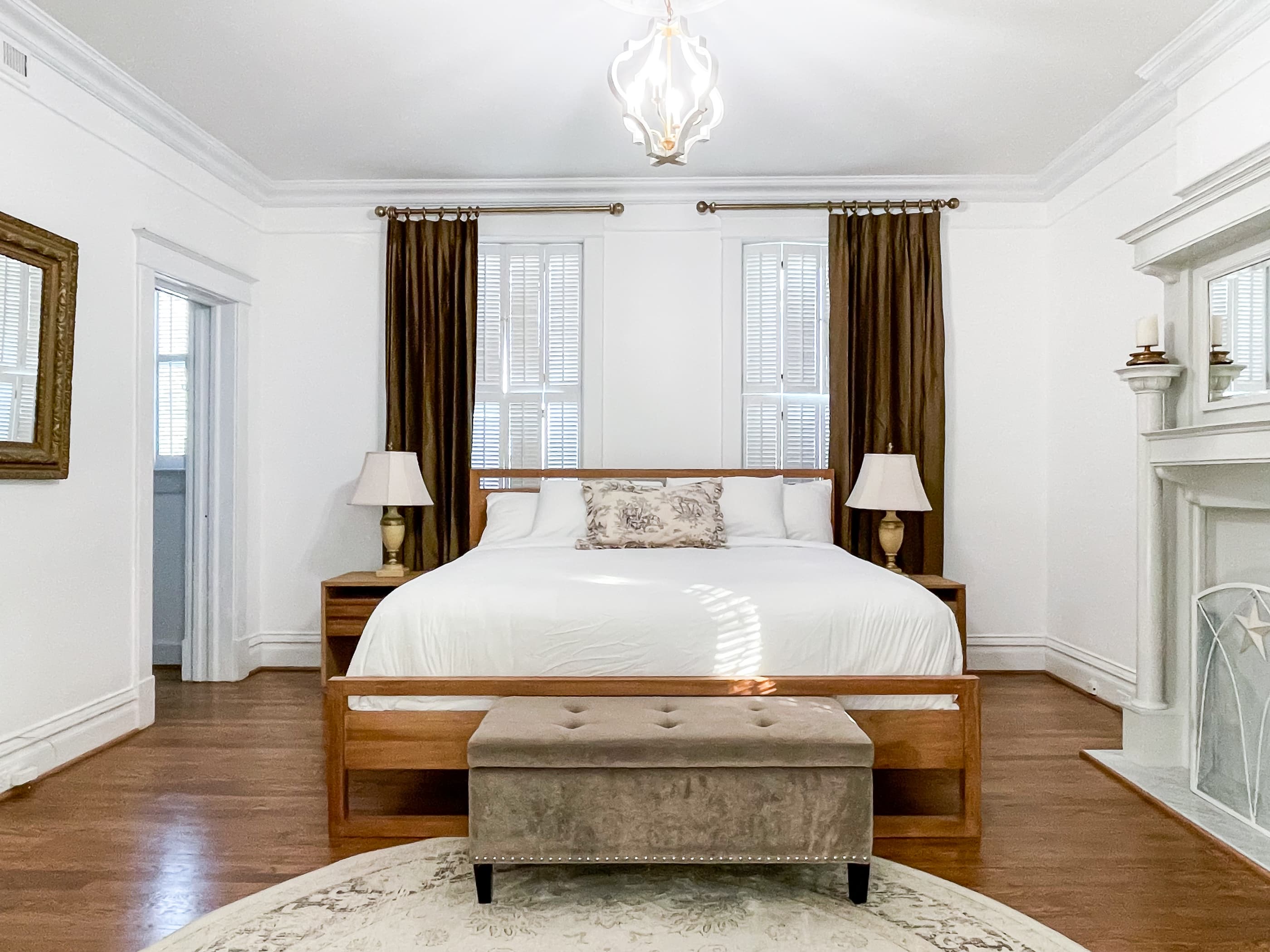 Mill Haus primary bedroom has a king size bed with crisp white linens, a nonworking fireplace accent, and an en suite bathroom with an amazing dressing room with delicious natural light.