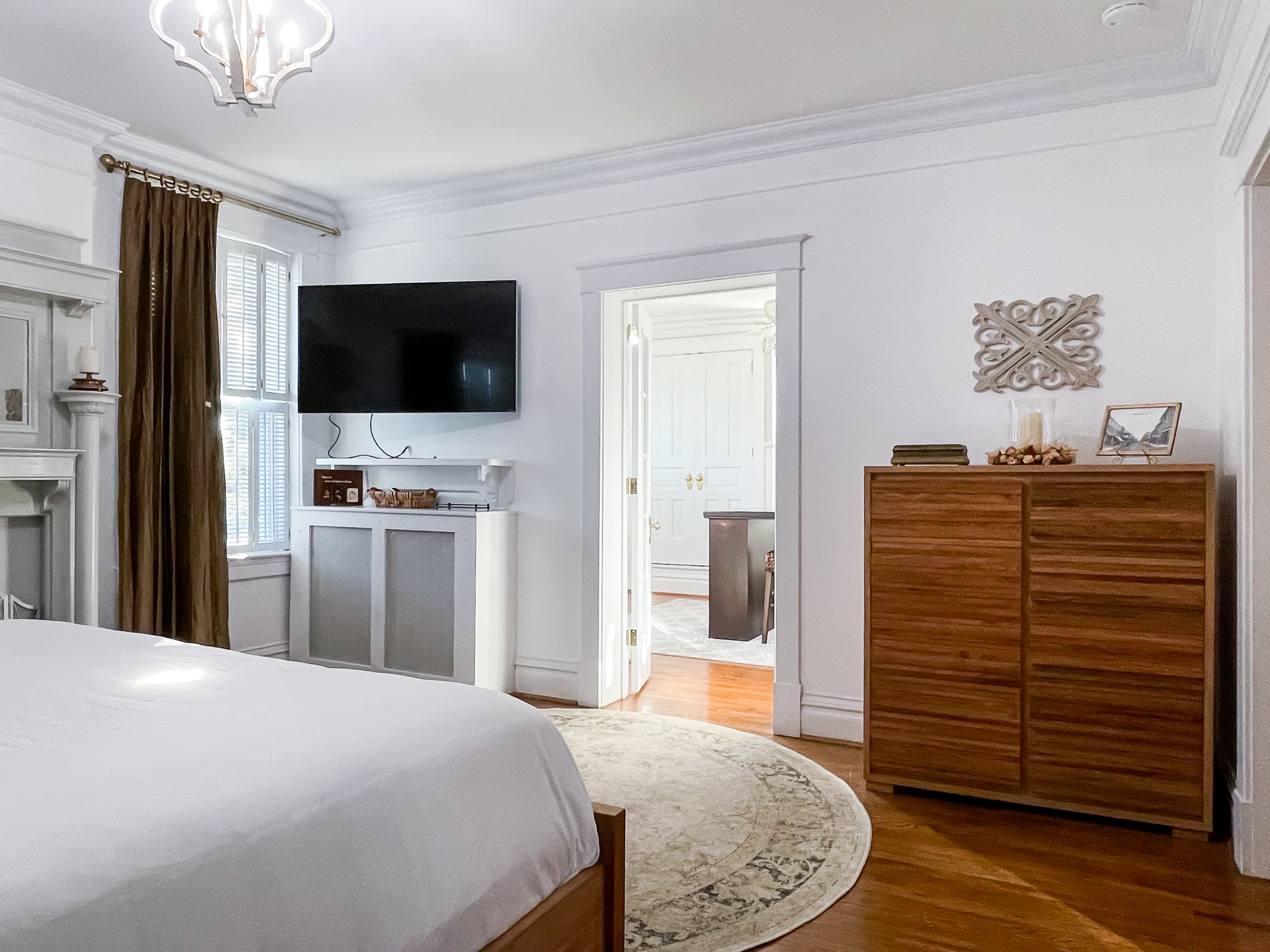 Mill Haus primary bedroom has a king size bed with crisp white linens, a nonworking fireplace accent, and an en suite bathroom with an amazing dressing room with delicious natural light.
