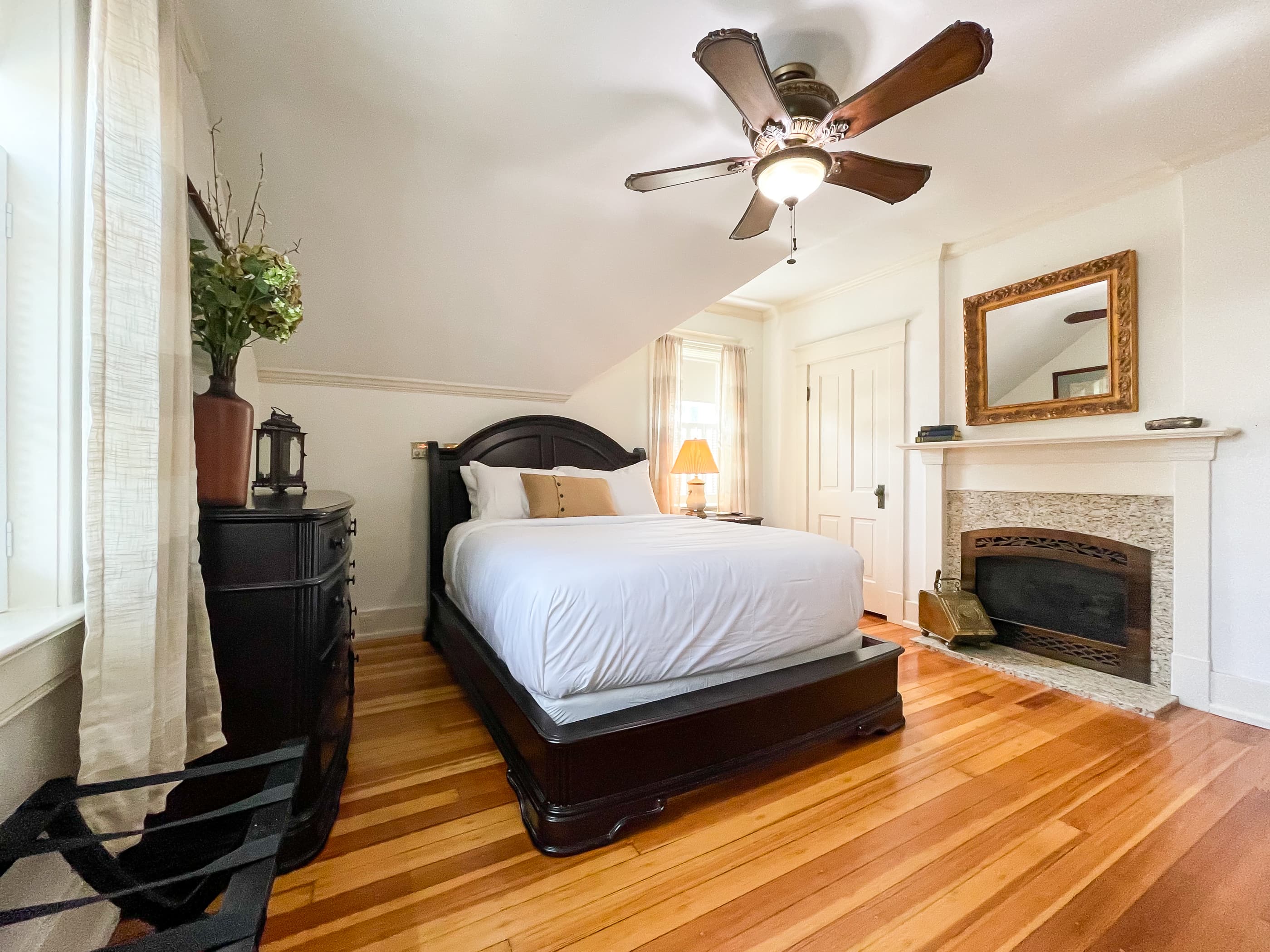 Spacious and airy primary queen bedroom with crisp white linens, a nonworking fireplace and an en suite bathroom with walk-in shower at The Beekeeper's Cottage.