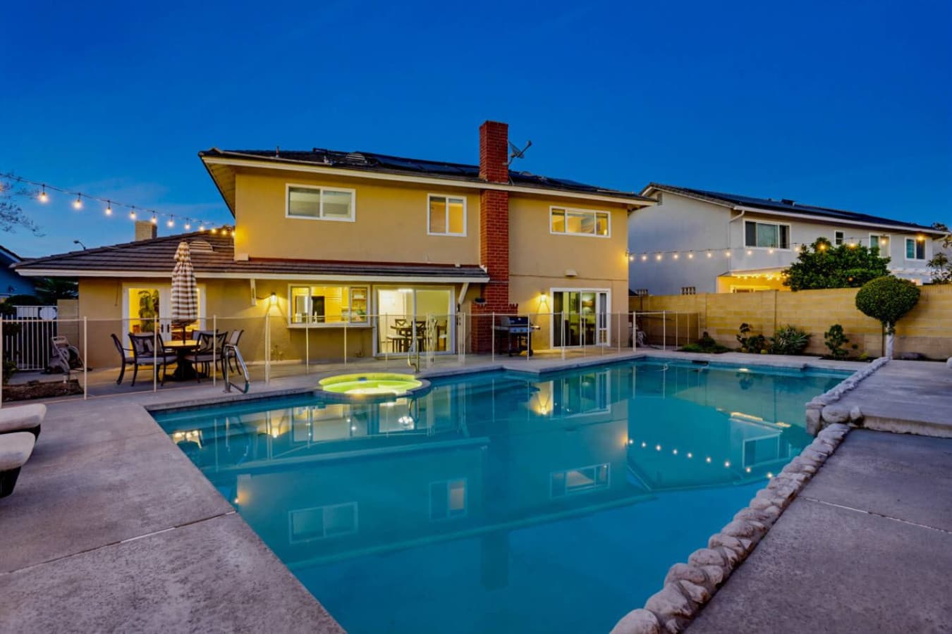Backyard pool glowing at dusk beside the home, creating a relaxing evening setting