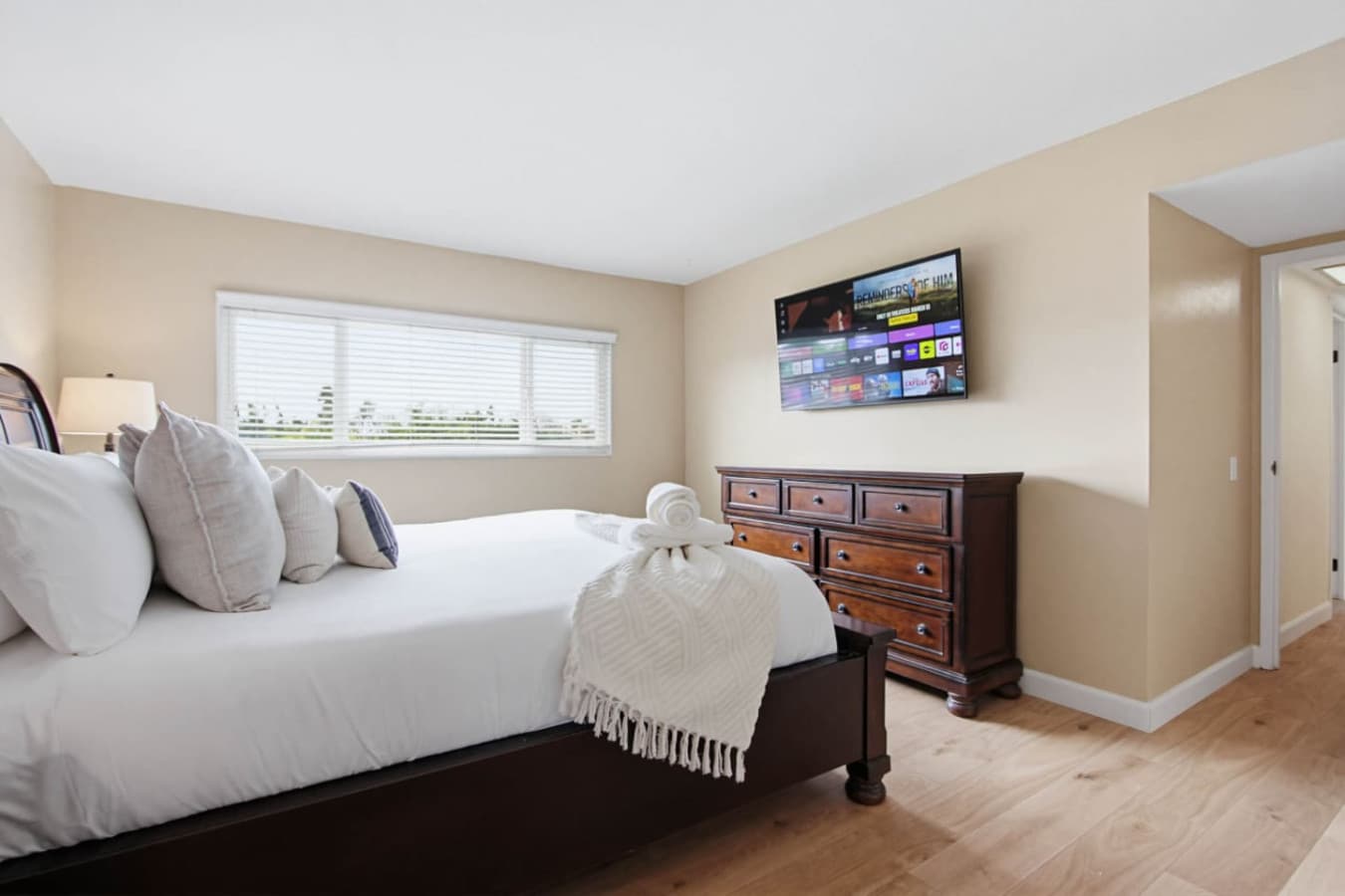 Bedroom w/ wall-mounted TV, wide dresser & bright windows for easy mornings & lazy evenings.