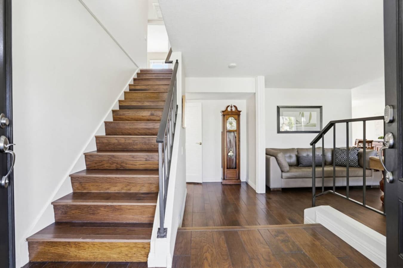 Hardwood staircase w/ iron railing leading down to the living room & grandfather clock.