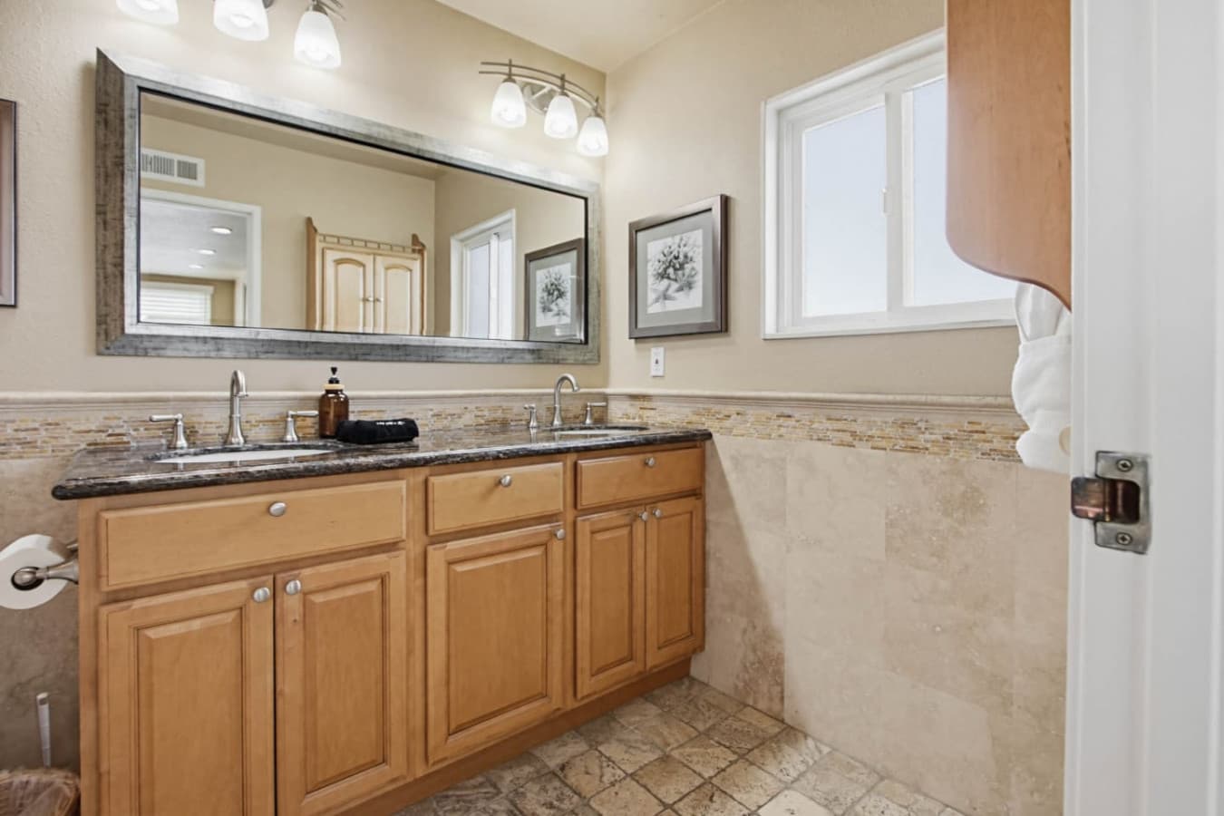 Bathroom w/ double vanity, granite counters & a wide framed mirror to speed up busy mornings.