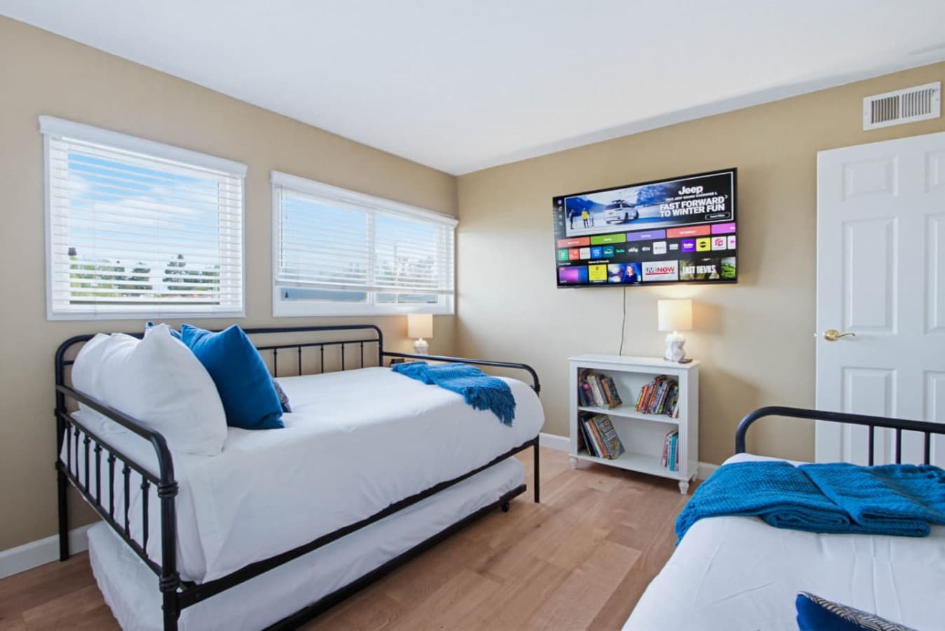 Guest room w/ two single beds, a wall-mounted TV & bookshelf for kids or extra guests.