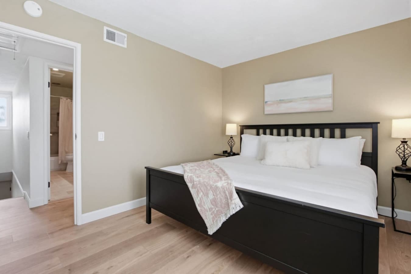 Bedroom w/ dark wood bed frame, matching lamps & a doorway through to the bath.