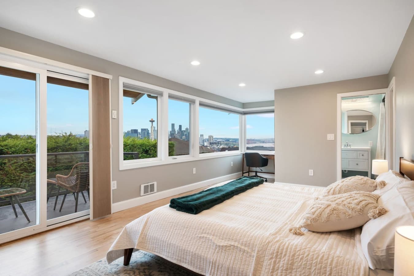 UPSTAIRS -MASTER BEDROOM & EN SUITE BATH: Combines comfort and elegance, a private patio with cozy seating and stunning Space Needle views, a dresser, smart TV, portable A/C, ceiling fans, workspace, and a queen-size bed with a bedside lamp.