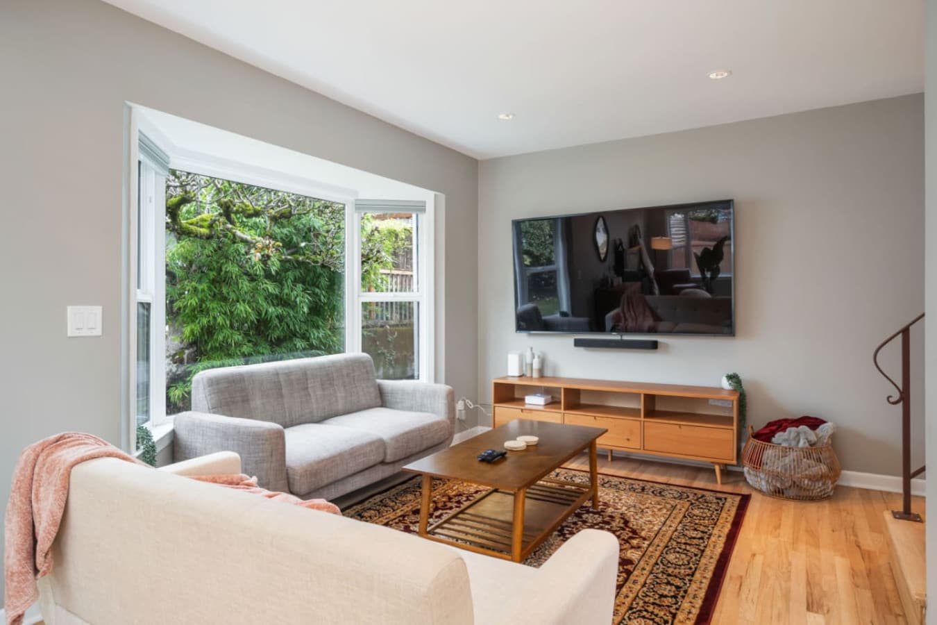 MAIN FLOOR - LIVING ROOM:  The inviting living room boasts large windows with lush views, a light gray sofa set for 2 people, a navy velvet love seat, and a Persian rug beneath a wooden coffee table.