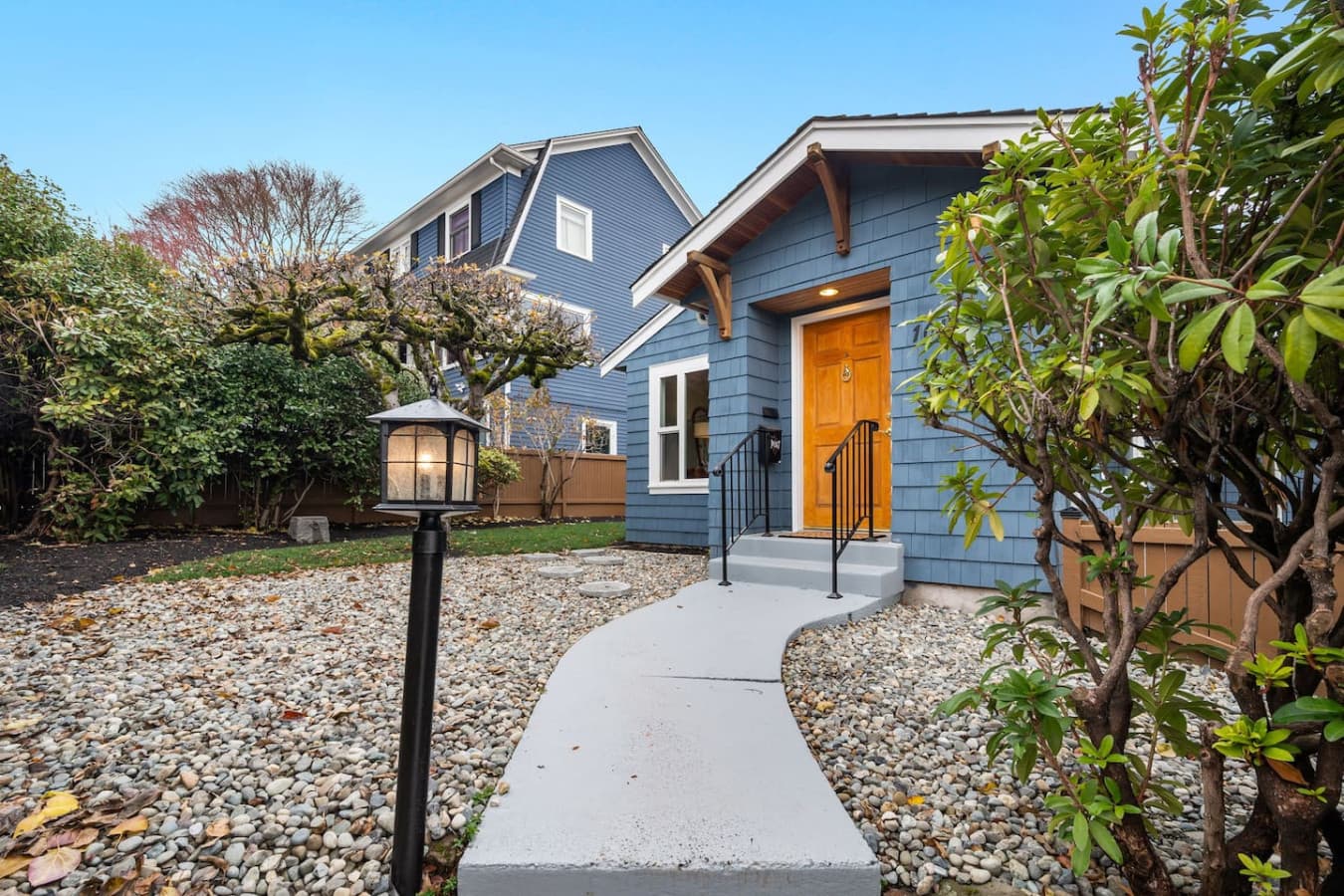 ENTRANCE: A charming entrance with a blue exterior, warm wooden door, and a peaceful stone pathway through a landscaped yard—inviting and cozy!