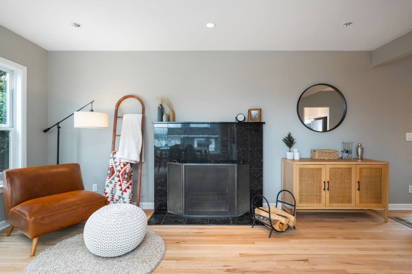 MAIN FLOOR : Unwind in the cozy corner featuring a black granite fireplace, a leather loveseat, blankets, and a modern sideboard with a bar setup that enhances the space.
