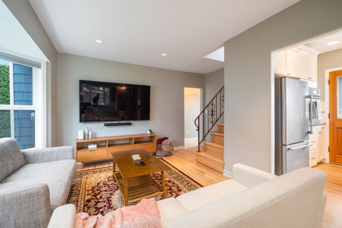 MAIN FLOOR - LIVING ROOM:  The inviting living room boasts large windows with lush views, a light gray sofa set for 2 people, a navy velvet love seat, and a Persian rug beneath a wooden coffee table.