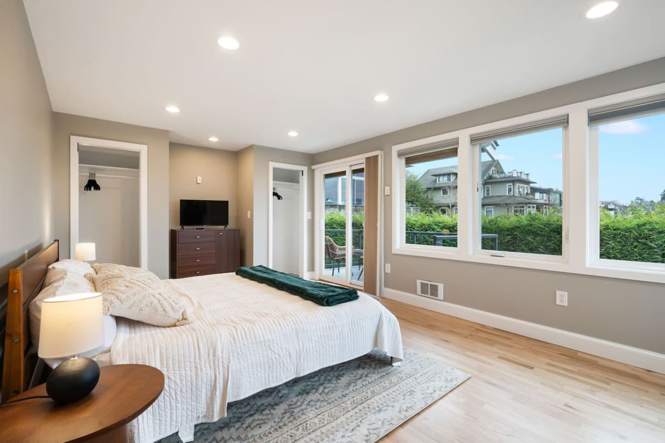 UPSTAIRS -MASTER BEDROOM & EN SUITE BATH: Combines comfort and elegance, a private patio with cozy seating and stunning Space Needle views, a dresser, smart TV, portable A/C, ceiling fans, workspace, and a queen-size bed with a bedside lamp.