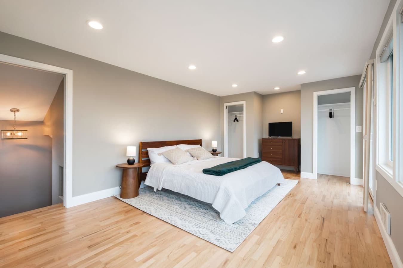 UPSTAIRS -MASTER BEDROOM & EN SUITE BATH: Combines comfort and elegance, a private patio with cozy seating and stunning Space Needle views, a dresser, smart TV, portable A/C, ceiling fans, workspace, and a queen-size bed with a bedside lamp.