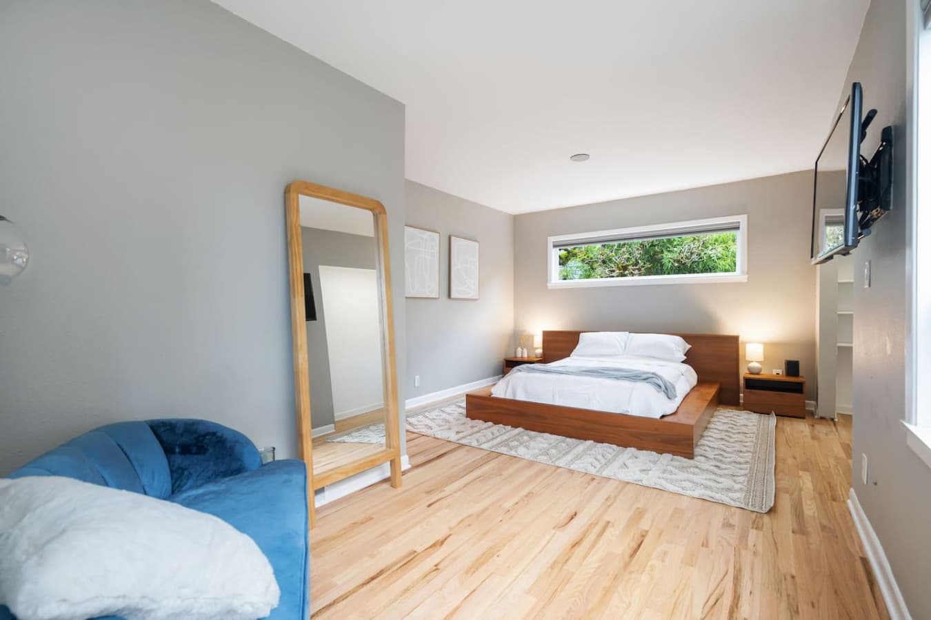 MAIN FLOOR - BEDROOM: The bedroom features a full-length mirror with a wooden frame, leaning against the wall next to the blue sofa. Its simple and elegant design enhances the room's minimalist aesthetic while also serving a practical purpose.