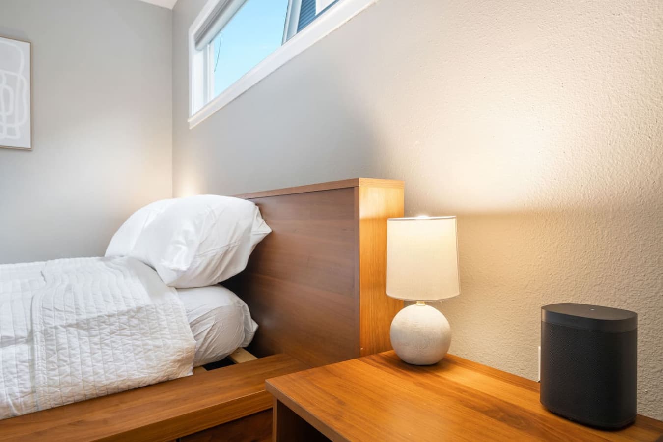 MAIN FLOOR-BEDROOM: A bed in a lower wooden style with a side table, featuring lamps and a Sonos One Smart Speaker Set of 2 Wi-Fi smart speakers with Alexa voice control.