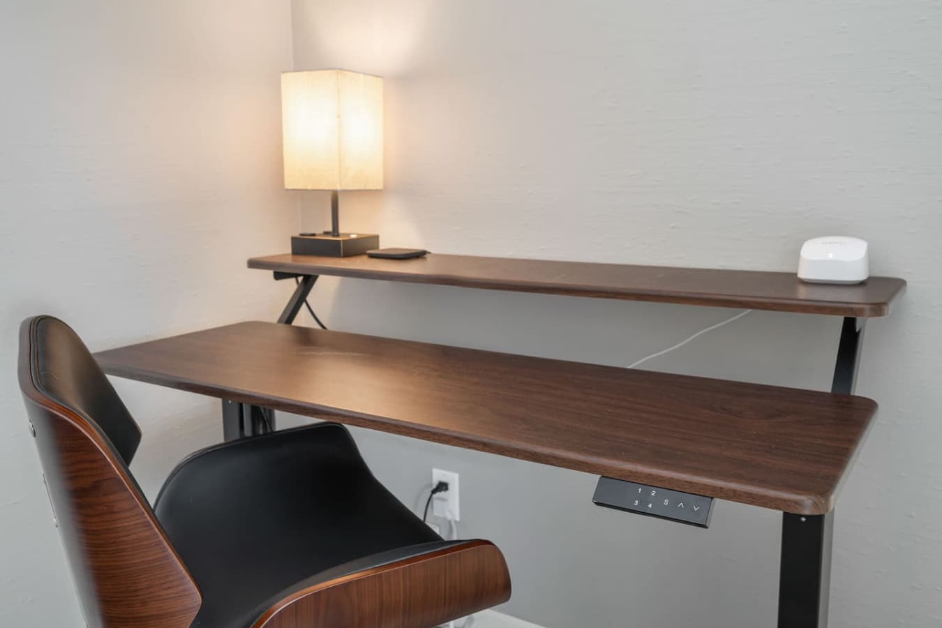 DOWNSTAIRS BEDROOM: Dedicated workspace with an electric height-adjustable desk and an ergonomic office chair.   Amazon eero 6 mesh wifi router and a lamp.