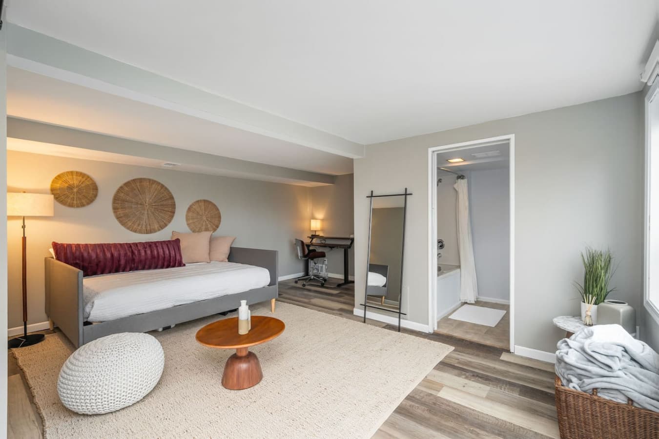 DOWNSTAIRS BEDROOM: A cozy room with a modern daybed, soft lighting, and a neutral palette. A large window brings in natural light, and an open closet adds convenience.