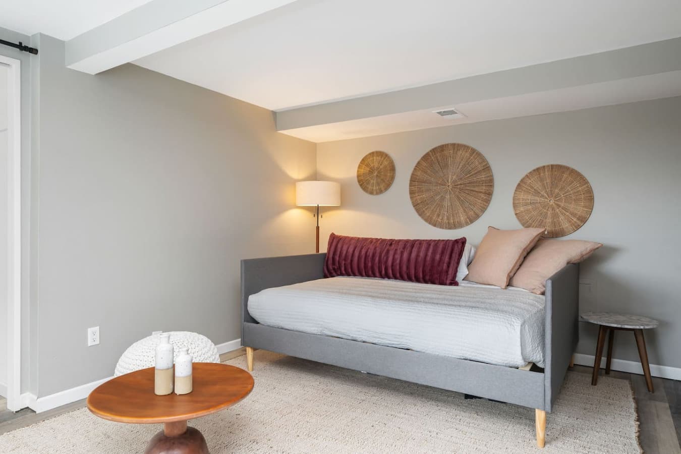 DOWNSTAIRS BEDROOM: A cozy room with a modern daybed, soft lighting, and a neutral palette. A large window brings in natural light, and an open closet adds convenience.