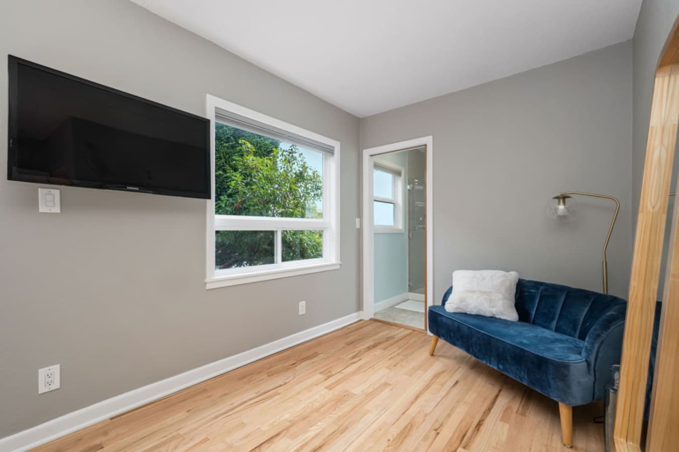 MAIN FLOOR - BEDROOM: The bedroom features a full-length mirror with a wooden frame, leaning against the wall next to the blue sofa. Its simple and elegant design enhances the room's minimalist aesthetic while also serving a practical purpose.