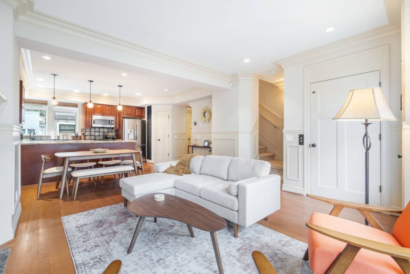A stylish open-concept space with a cozy living area, dining table, and a well-equipped kitchen. The staircase to the second floor is located behind the sofa.