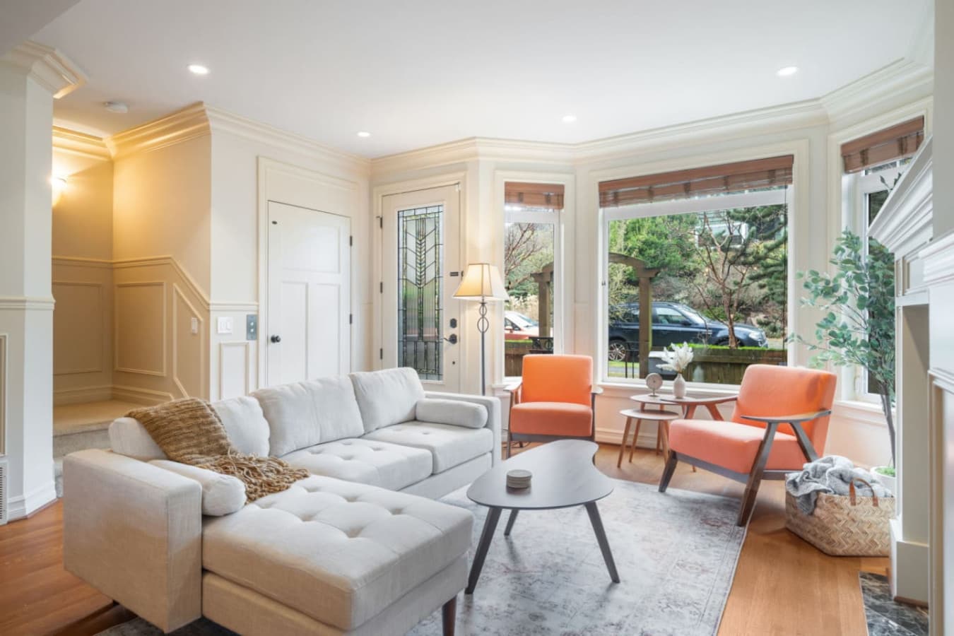 Natural light streams in through the large windows, which have wooden blinds and offer a view of the lush outdoor area.