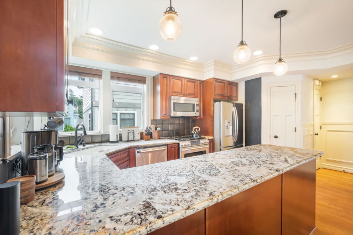 The kitchen features cherry wood cabinets, granite countertops, and a central island. Stainless steel appliances include a double-door fridge, gas stove, microwave, and dishwasher.