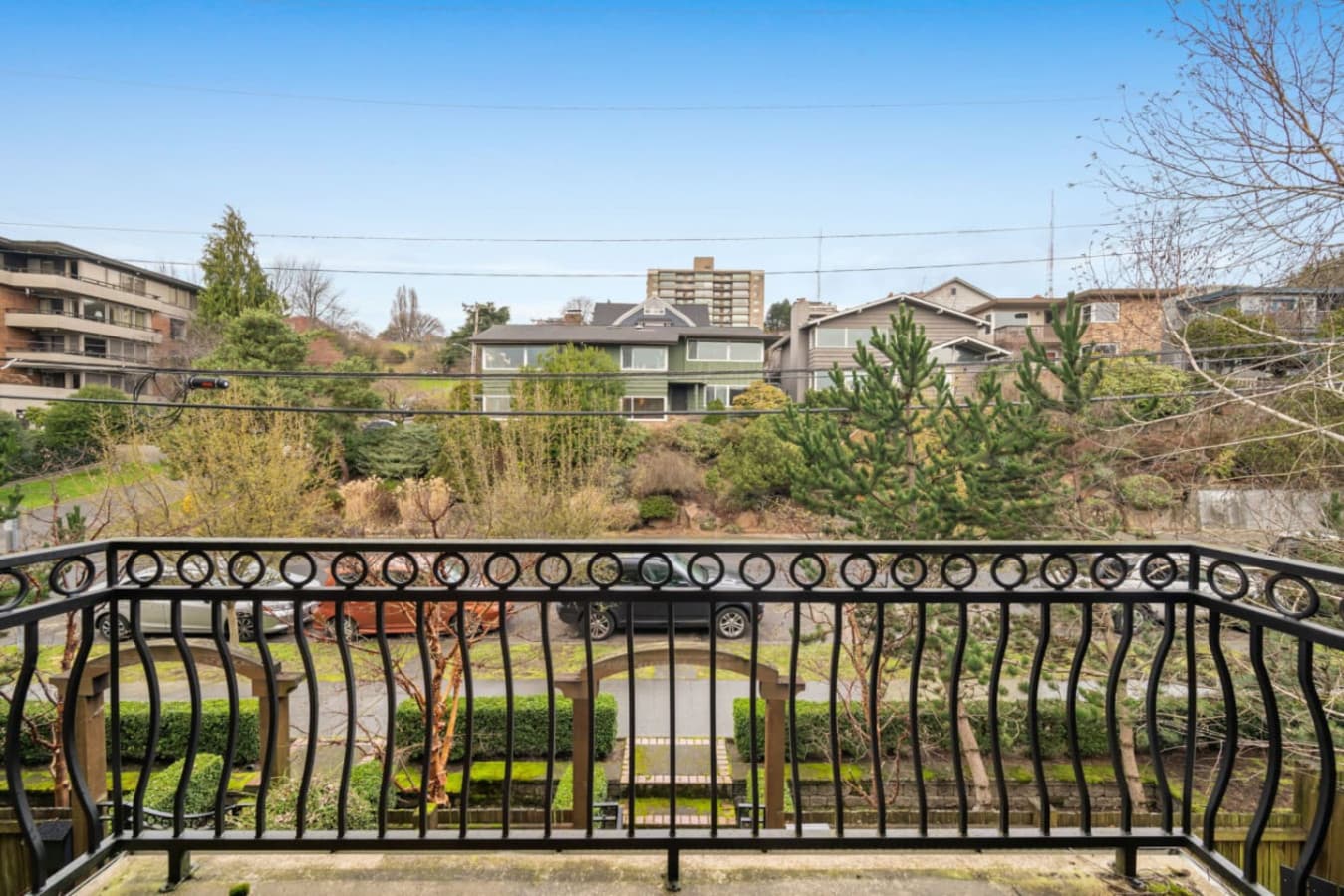 This is a cozy balcony with elegant wrought iron railings, offering a pleasant view of a quiet residential street. The surrounding area features lush greenery, well-maintained gardens, and a mix of modern and traditional homes.
