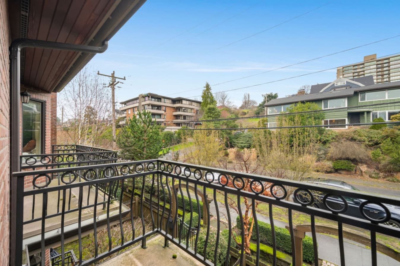 This is a cozy balcony with elegant wrought iron railings, offering a pleasant view of a quiet residential street. The surrounding area features lush greenery, well-maintained gardens, and a mix of modern and traditional homes.
