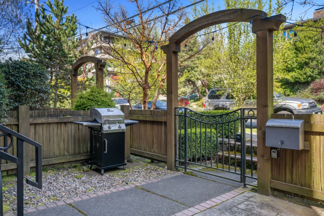Step into a charming outdoor retreat, framed by elegant wooden arches and a wrought iron gate. This private patio offers a serene space to unwind, featuring a grill for delightful outdoor cooking.