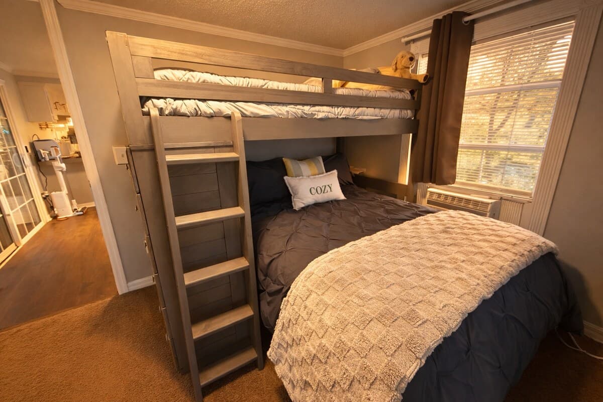 A cozy, space-smart bedroom featuring a twin-over-full bunk bed, perfect for families or friends. Soft lighting, comfortable bedding, and a window AC unit keep the room cool and restful after a full day of exploring.