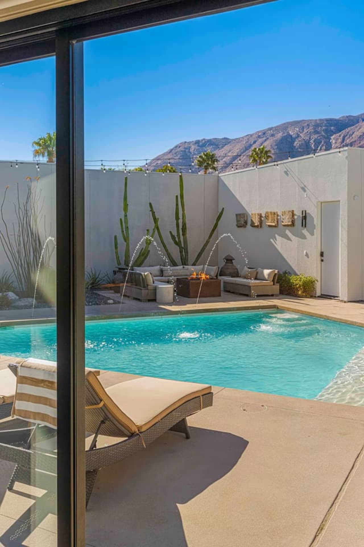 Serene poolside corner w/ built-in seating, fire feature, and desert greenery for relaxed evenings outside.