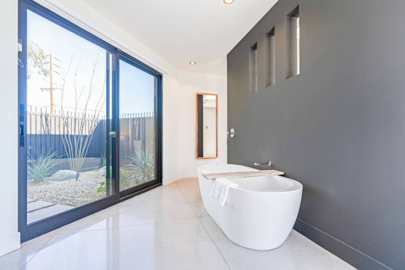 Bright spa-like bath w/ freestanding tub, matte finishes, and large windows bringing in desert light.