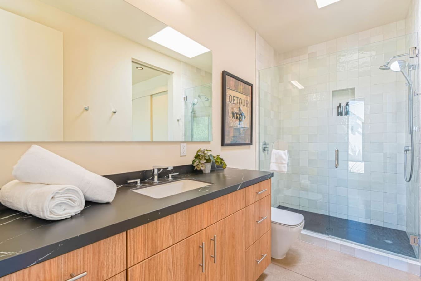 Spacious bathroom w/ a long vanity, walk-in shower, and skylight that fills the space w/ natural light.