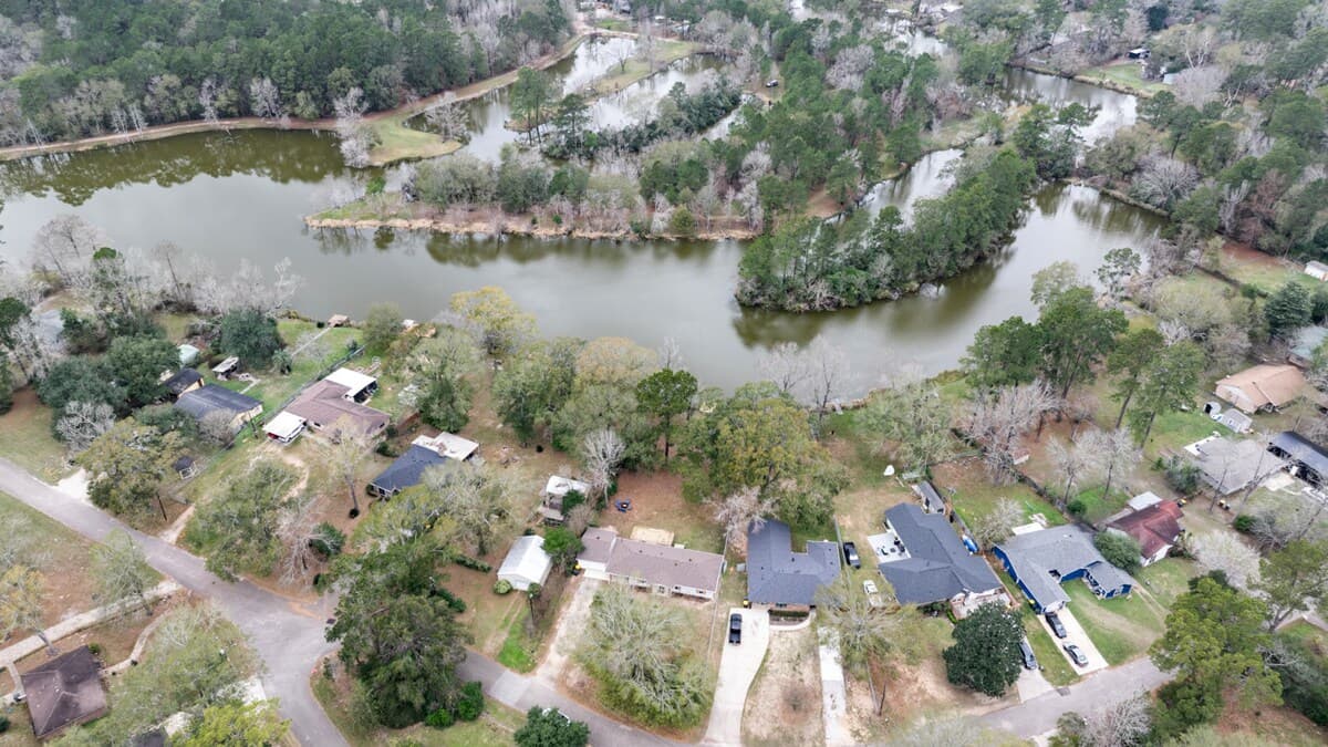Aerial view of this stunning lakefront home, surrounded by lush, tree-lined scenery—showcasing peaceful waterside living just steps from nature while staying close to the neighborhood.