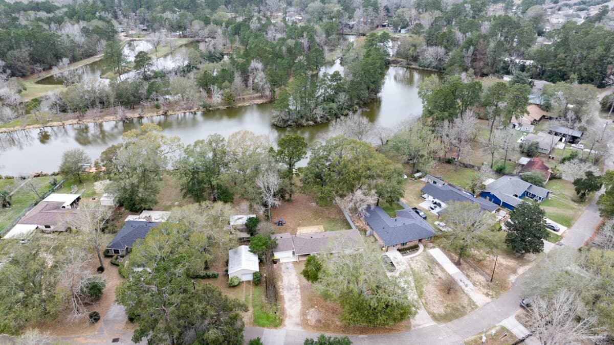 Aerial view of the peaceful, tree-lined neighborhood with serene waterfront lake just steps from the home—perfect for morning walks, fishing, or unwinding in nature while staying close to local conveniences.