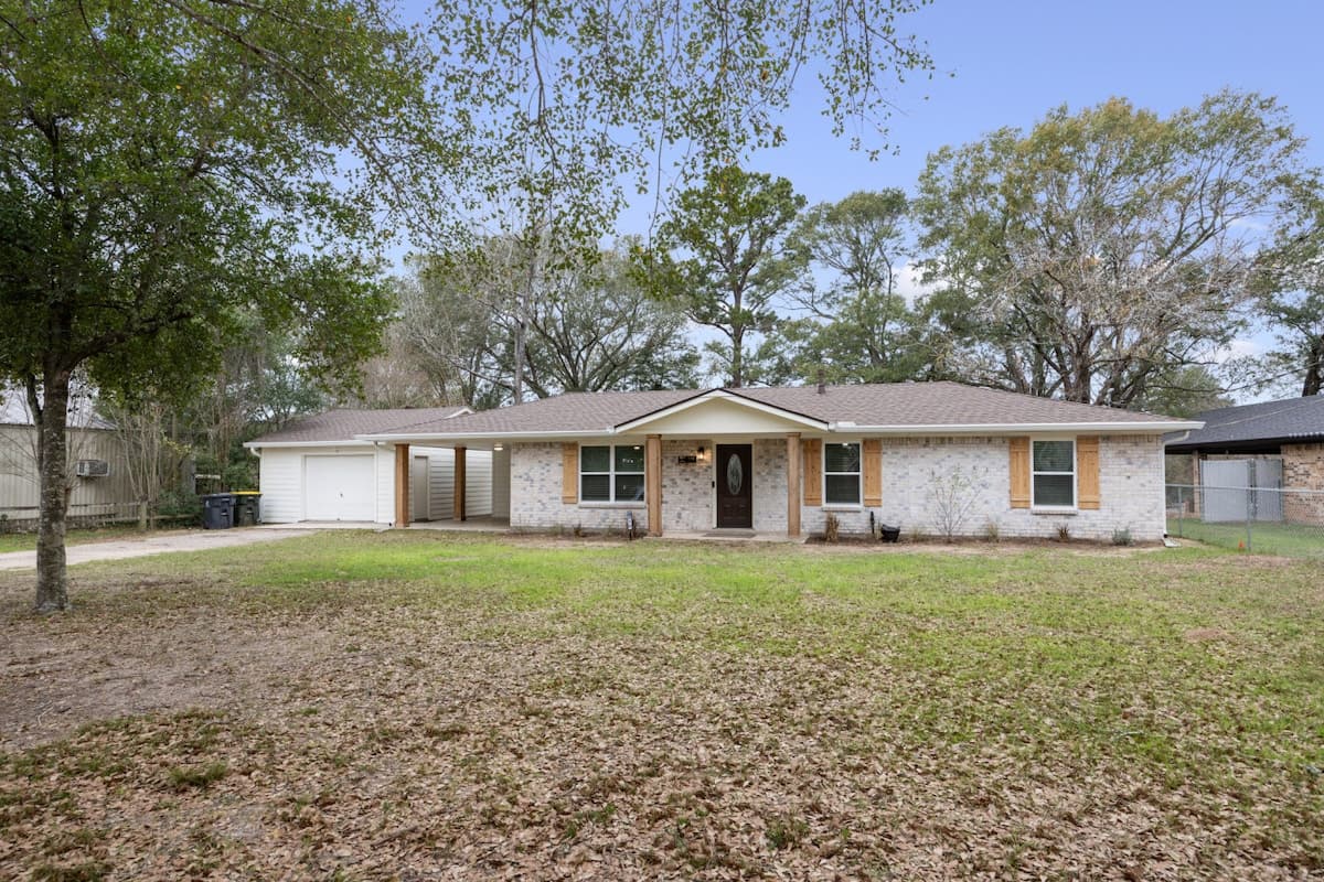 Wide front view showcasing the brick exterior, clean lines, and generous open yard, framed by mature trees for a peaceful, spacious feel.