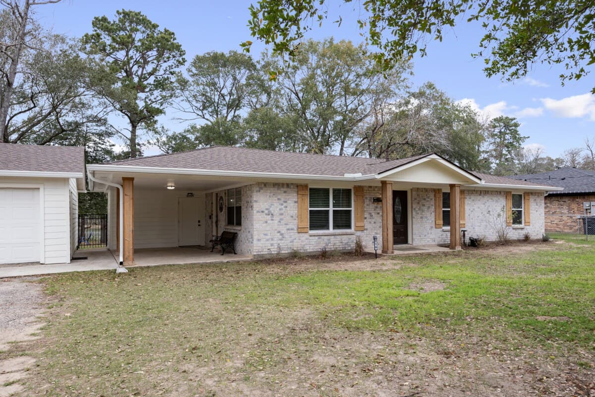 Single-story brick home with a covered front porch, carport access, and mature trees creating a quiet, private setting.