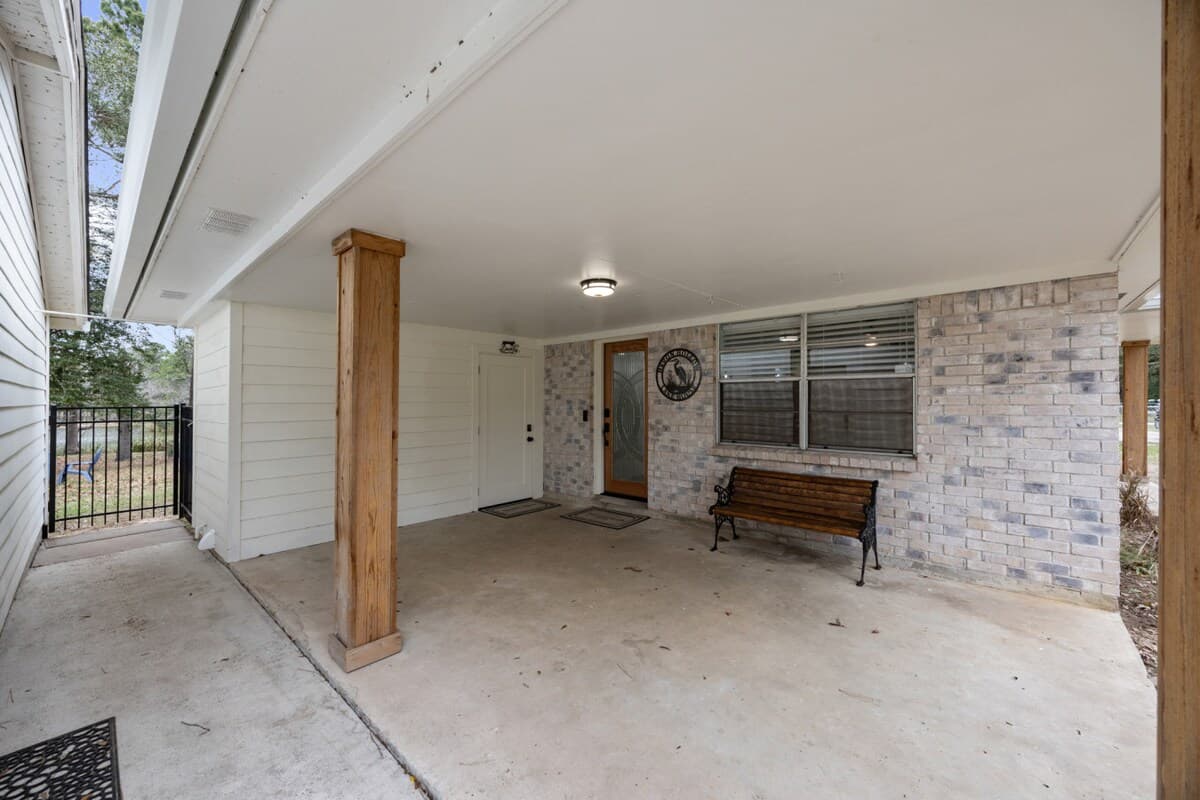 Covered front porch with a shaded concrete patio, wood posts, and a bench—an easy spot to arrive, unwind, or enjoy a quiet moment outside.