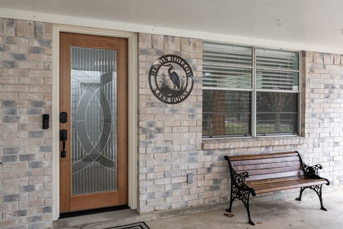 Welcoming brick entry with a decorative glass front door and cozy bench—setting the tone for the Heron Hollow Lakehouse experience.