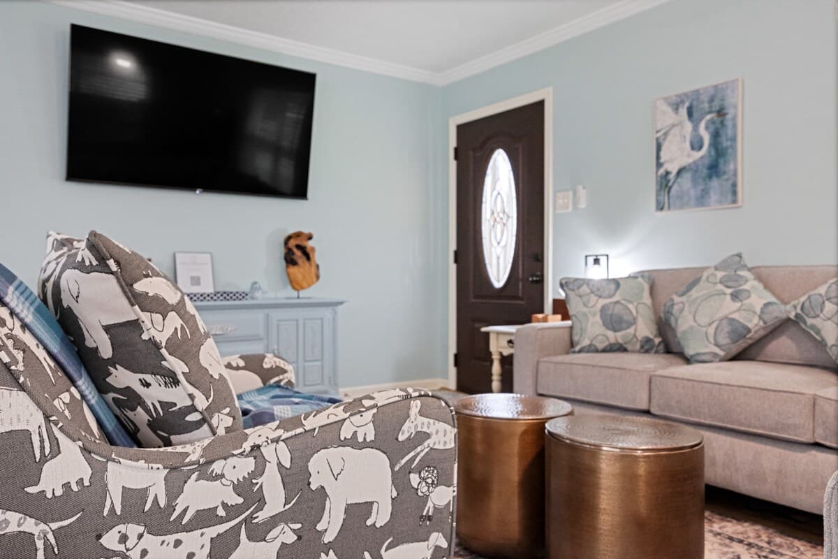 Living room view with comfortable seating, accent chairs, and a mounted 65" TV—perfect for movie nights or relaxing together.