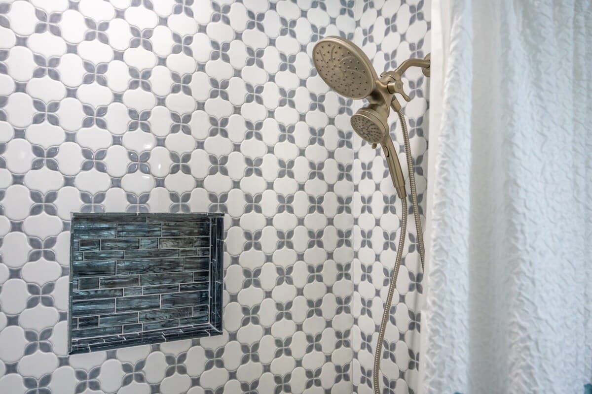 Detailed shower view featuring patterned tile, built-in niche, and a handheld shower head for added convenience.