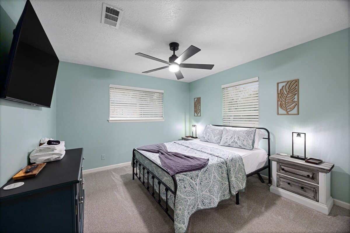 Comfortable guest room with a queen bed, ceiling fan, and 55" TV—ideal for a relaxing and restful stay.