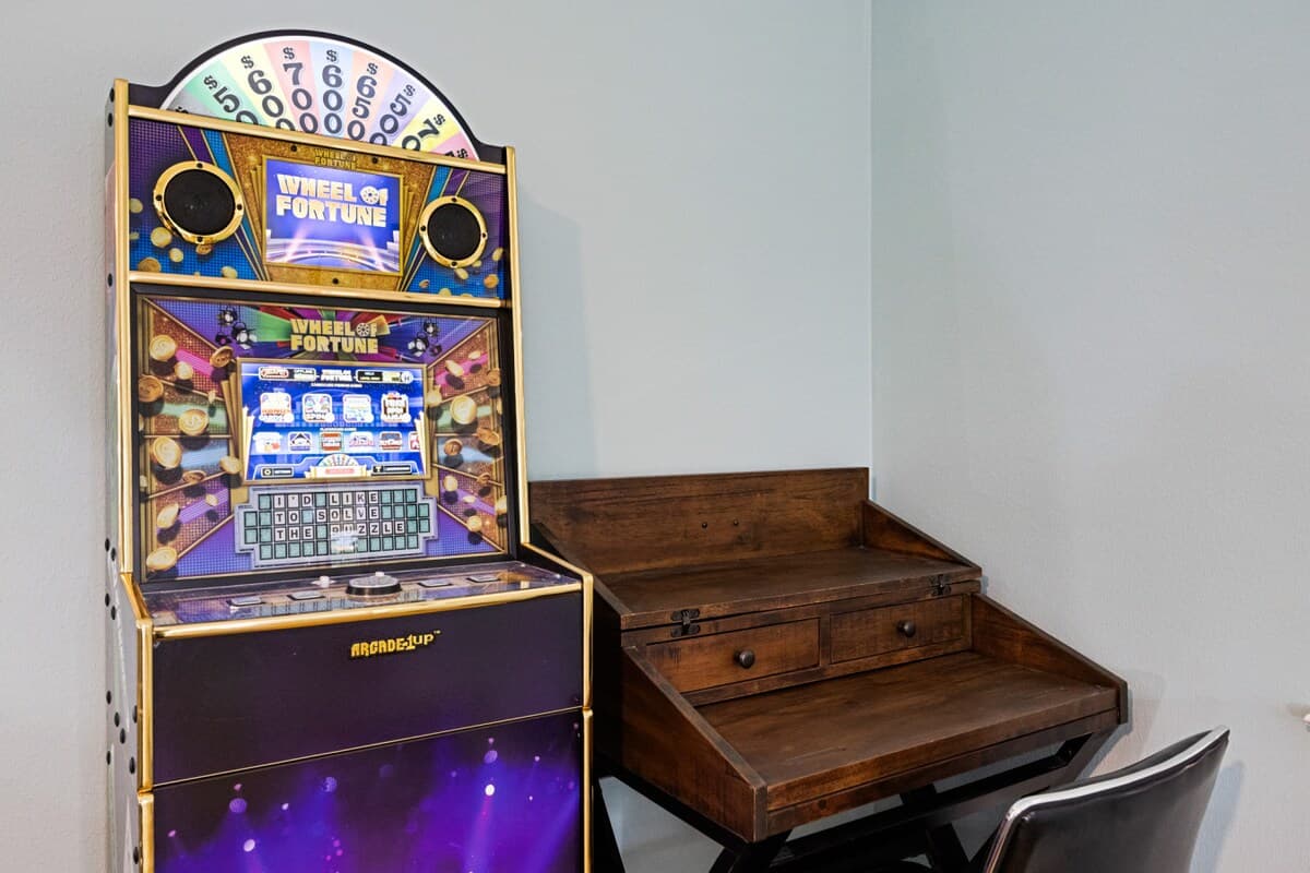 Corner featuring a Wheel of Fortune arcade game alongside a practical desk—perfect for work, study, or play.