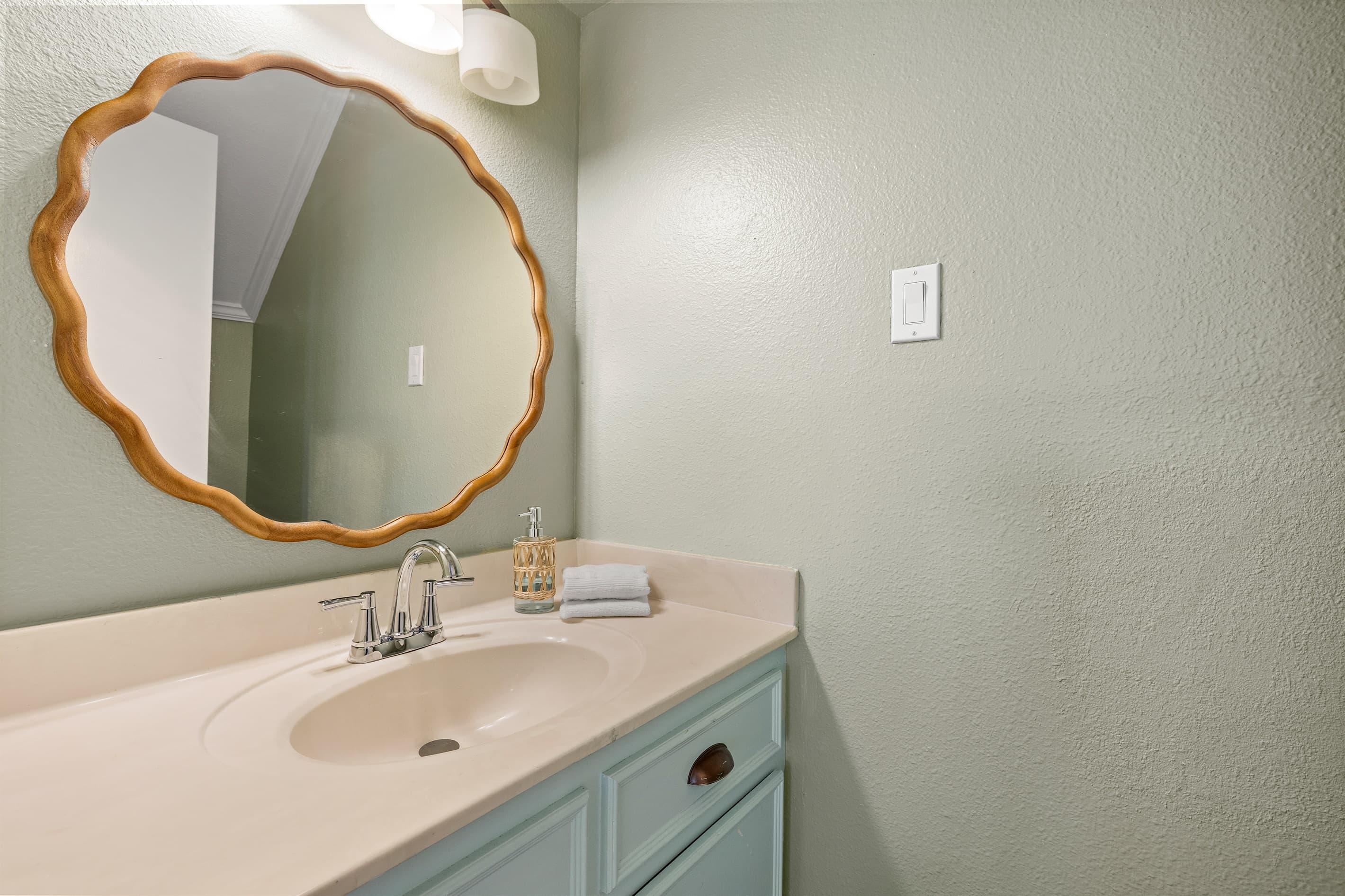 Stylish half bath at Lakeview Landing — designer scalloped gold mirror and sage green accents bring character to the downstairs powder room.