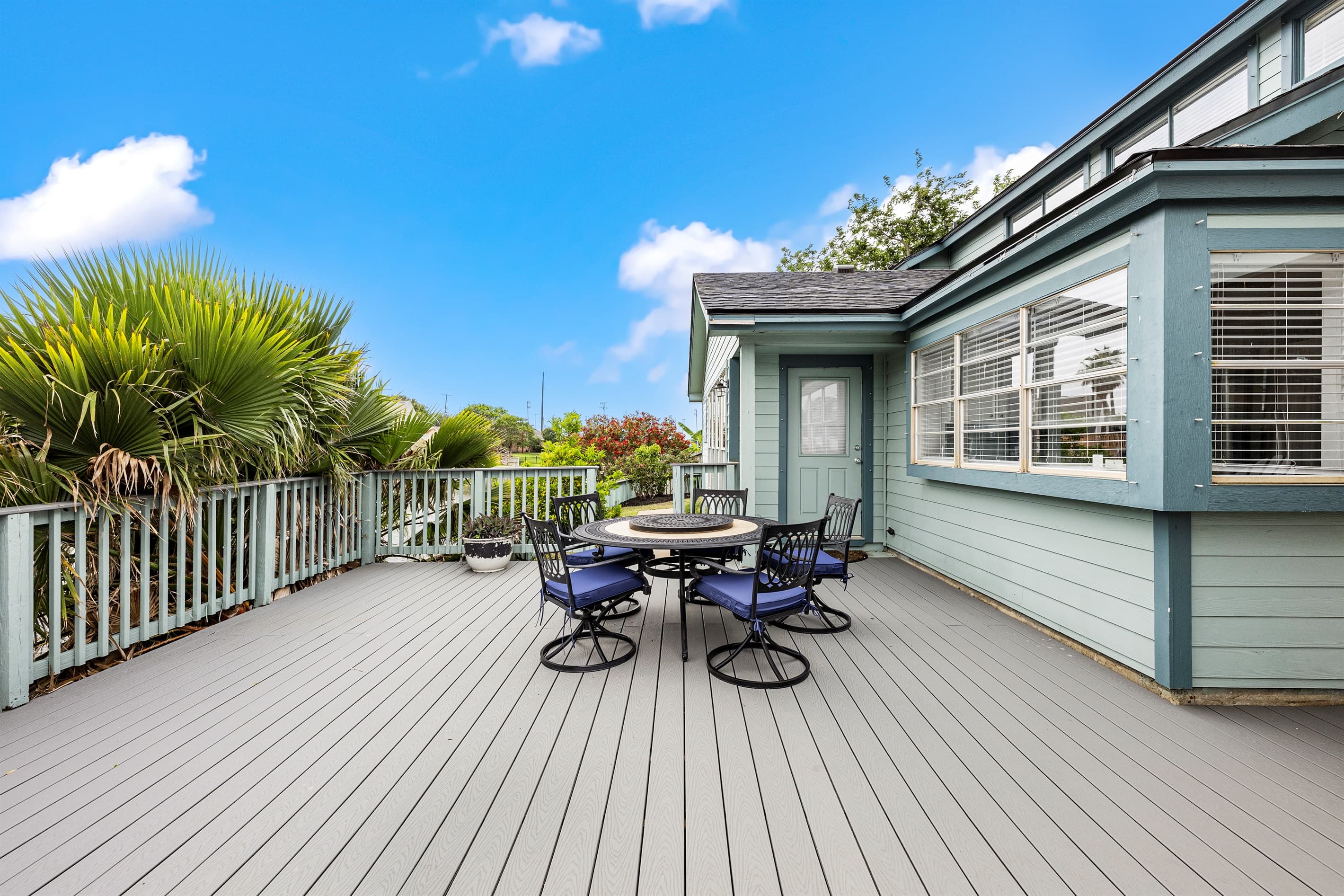 Outdoor dining on the deck at Lakeview Landing — round table seating beneath a Galveston blue sky, with Madeline Lake just steps away.