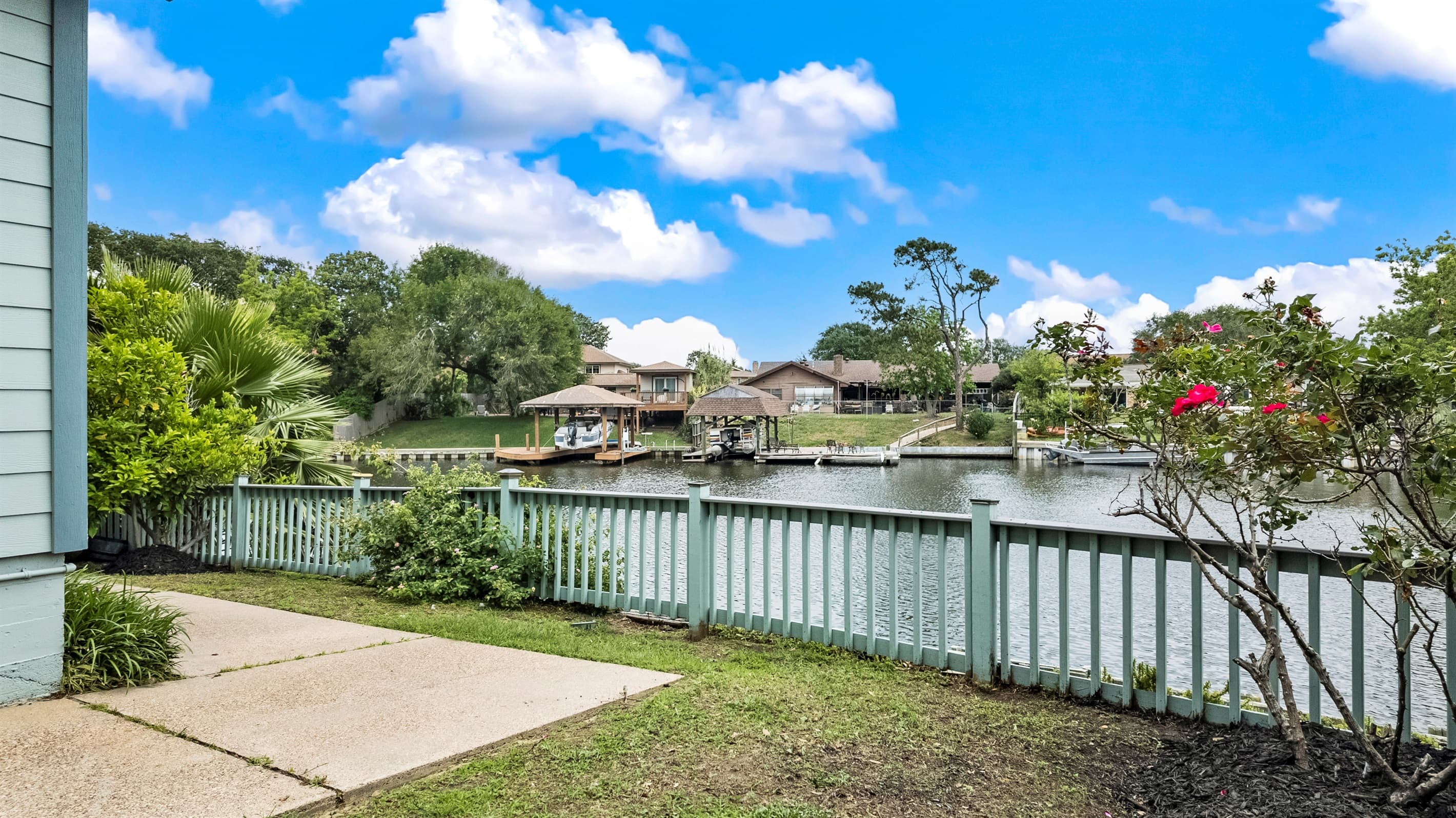 Deck railing views at Lakeview Landing — Madeline Lake stretches beyond colorful blooms, a picture-perfect Galveston waterfront moment.