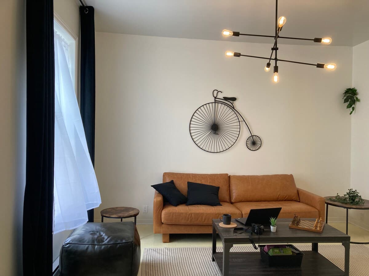 Bright and stylish living room with mid-century charm, leather sofa, smart TV, chic decor, and a cozy vibe—perfect for relaxing, working remotely, or enjoying a game night. Air-conditioned and filled with natural light for year-round comfort.